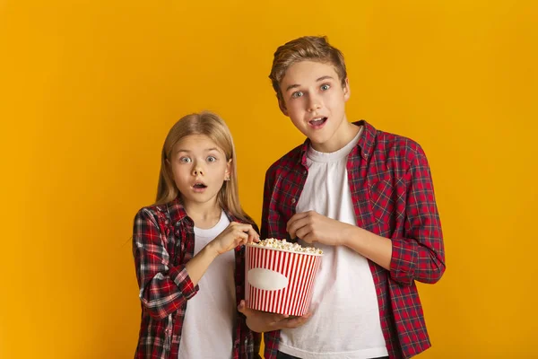 Geschockte Geschwister essen Popcorn und öffnen staunend den Mund — Stockfoto