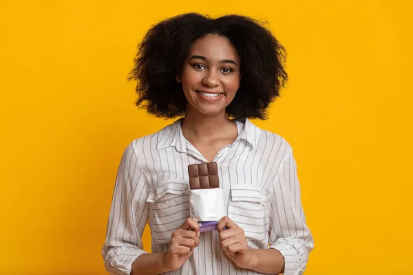 Söt svart flicka med mjölk choklad bar Posing över gul bakgrund — Stockfoto