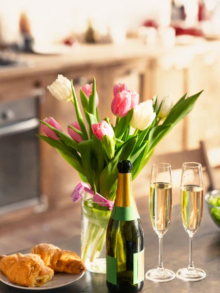 Buquê de tulipas de primavera, champanhe e croissants na mesa na cozinha — Fotografia de Stock