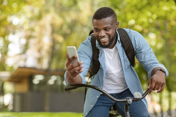 Szczęśliwy czarny człowiek jazda na rowerze na zewnątrz i za pomocą smartfona — Zdjęcie stockowe