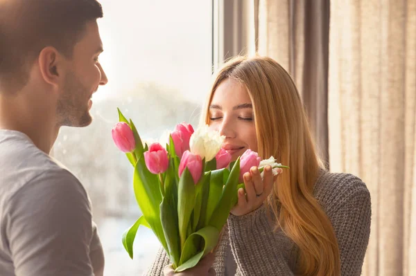 Affettuoso giovane uomo che presenta mazzo di fiori a sua moglie a casa — Foto Stock