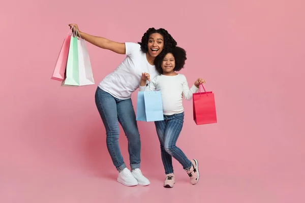 Gelukkig zwart moeder en dochter poseren met winkelen tassen, roze achtergrond — Stockfoto