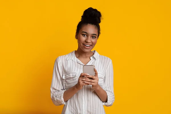Femme afro excitée avec Smartphone dans les mains posant sur fond jaune — Photo