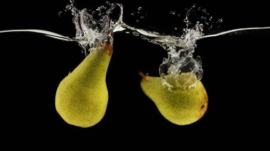 İki sulu armut, berrak sulara dökülüyor. Siyah arka planda sıçrama var. Panorama.