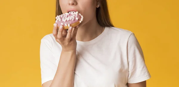 Tanınamayacak kadar aç olan kız donut yiyor, sarı arka planda tatlılar için açlıktan ölüyor. — Stok fotoğraf