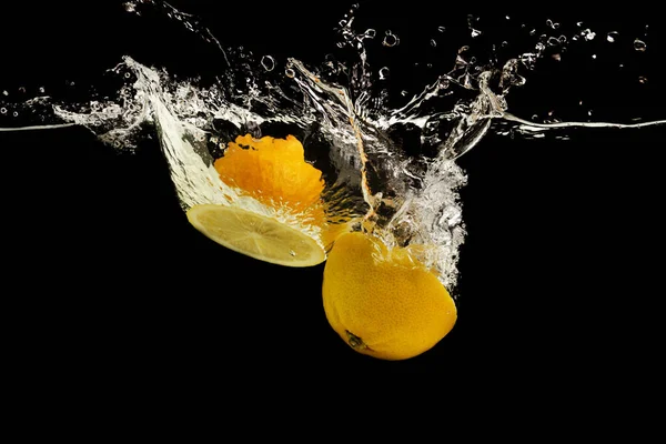 Lemon halves falling deeply under water on black background — Stock Photo, Image