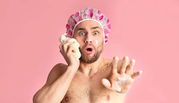 Наляканий хлопець в душовій шапці натирає обличчя губкою — стокове фото