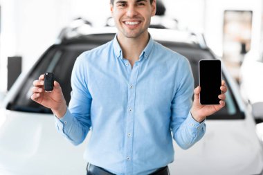 Satış merkezinde araba anahtarı ve akıllı telefon gösteren bir adam var.