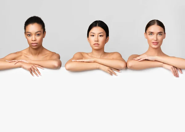 Drie multi-etnische dames poseren achter witte boord in de studio — Stockfoto