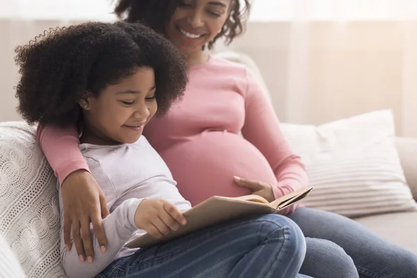 Hamile anne ve küçük afro kızı birlikte ilginç bir kitap okuyorlar. — Stok fotoğraf
