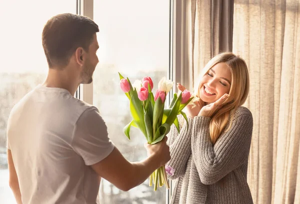 Jovem romântico apresentando flores para sua namorada em casa — Fotografia de Stock