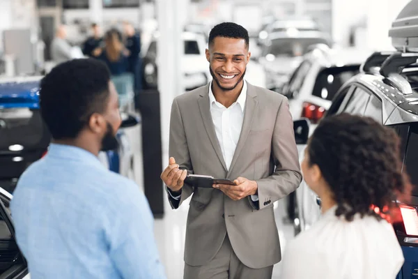 Negociante profissional conversando com clientes que mostram automóveis na loja de concessionárias — Fotografia de Stock