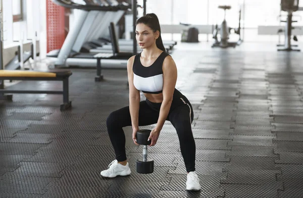 Ung kvinna med hantel gör knäböj i gymmet — Stockfoto