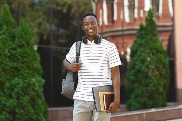 Feliz chico africano estudiante con mochila y libros de trabajo sobre fondo universitario —  Fotos de Stock