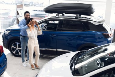 Husband Covering Wifes Eyes Showing New Auto In Dealership Store