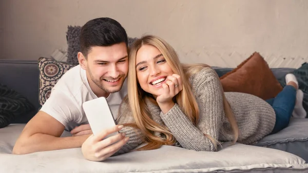 Milující mladý pár s mobilním telefonem ležící na pohovce doma — Stock fotografie