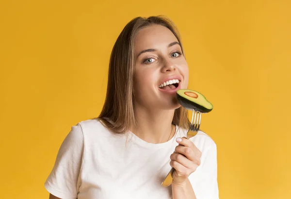 Grasas saludables. Mujer feliz comiendo aguacate mitad y mirando a la cámara — Foto de Stock