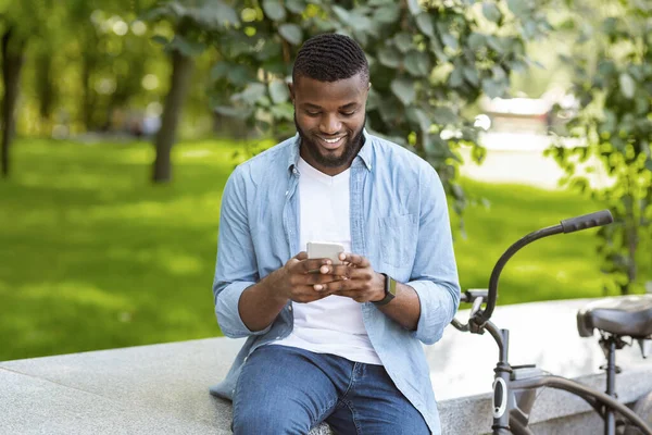 Homem negro feliz em roupas casuais mensagens de texto no smartphone ao ar livre — Fotografia de Stock