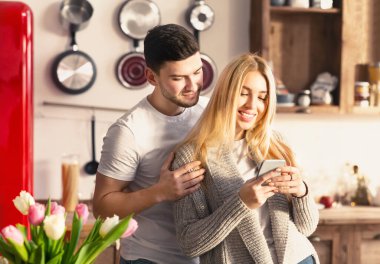 Affectionate millennial couple with mobile phone in kitchen