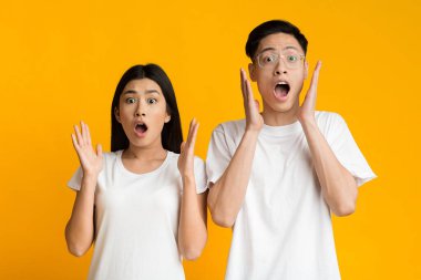 Amazed young asian couple expressing shock, yellow background