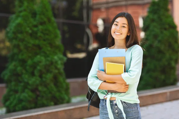 Asiática estudiante chica con mochila y cuadernos de pie sobre fondo universitario — Foto de Stock