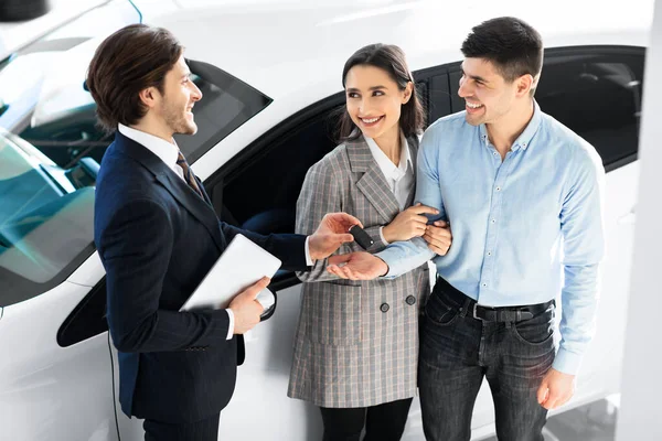 Couple Taking Key From Salesman In Auto Showroom — Stock Photo, Image