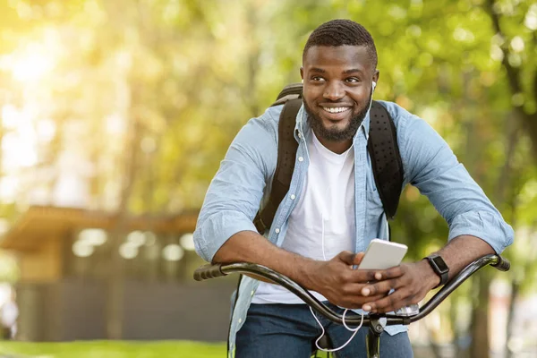 Happy Afro Man siedzi na rowerze i słuchanie muzyki na smartfonie — Zdjęcie stockowe