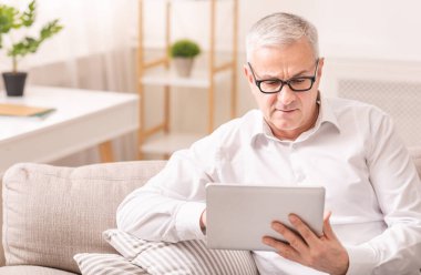 Senior man using digital tablet sitting on sofa