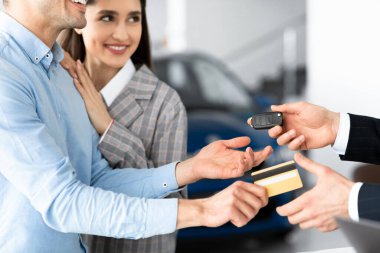 Couple Buying Car Giving Seller Credit Card In Dealership Office
