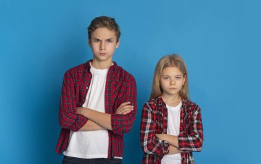 Siblings Conflicts. Frowning Little Brother And Sister Standing With Folded Arms