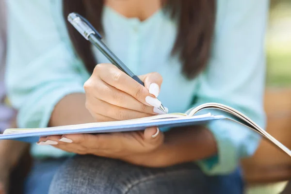 Onherkenbare vrouwelijke student die buiten zit, notities maakt, close-up — Stockfoto