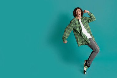 Cheerful young man standing on tiptoes against color background, empty space