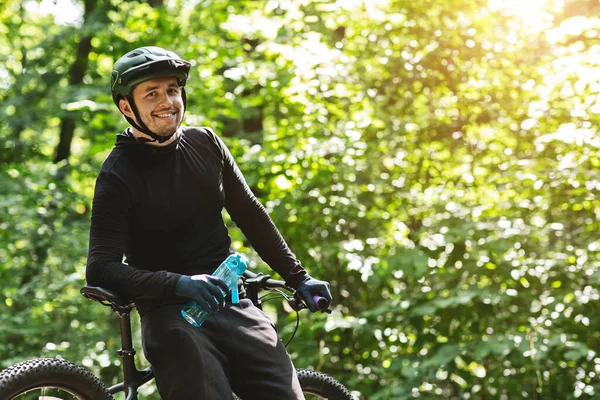 Szczęśliwy rowerzysta trzymający butelkę wody, uśmiechnięty do kamery — Zdjęcie stockowe
