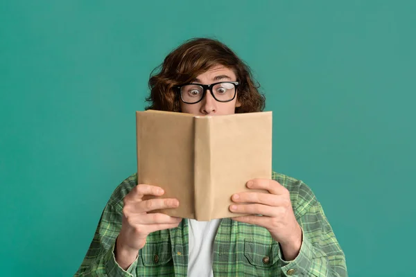 Eğitim konsepti. Kafası karışmış, gözlüklü, arka planda renk kitabı okuyan bir genç. — Stok fotoğraf