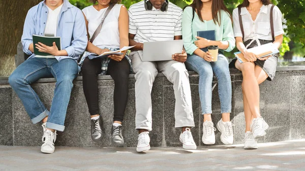 Divergir estudantes universitários sentados ao ar livre com laptop e cadernos de trabalho, estudando juntos — Fotografia de Stock