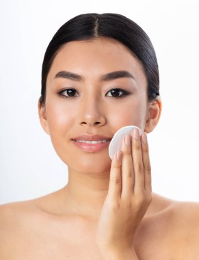 Asian Girl Using Cotton Pad Smiling At Camera, White Background