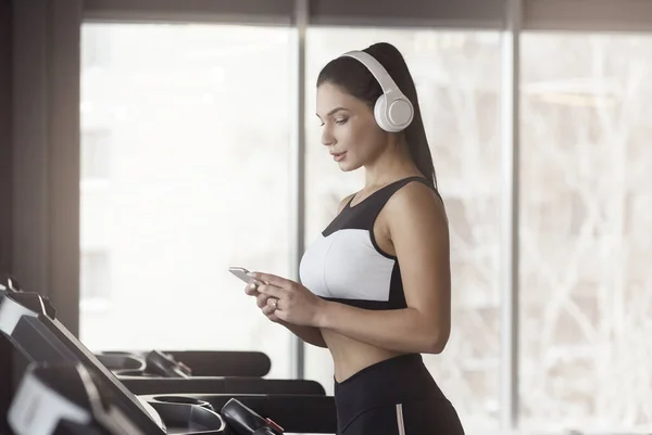 Menina encantadora com smartphone e fones de ouvido ouvindo música na esteira rolante, espaço de cópia — Fotografia de Stock