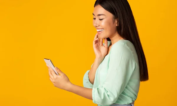 Smiling Chinese Girl Holding Smartphone Reading Message, Studio Shot — Stockfoto