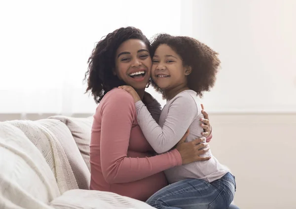 Adorable niña negra abrazando a la madre embarazada y riéndose en casa —  Fotos de Stock