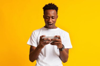 Excited african guy holding cellphone and playing video games