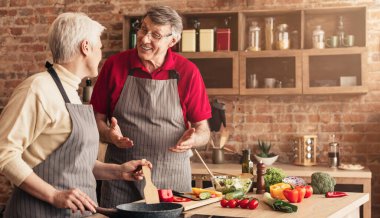 Cheerful aged couple enjoying cooking in kitchen together,
