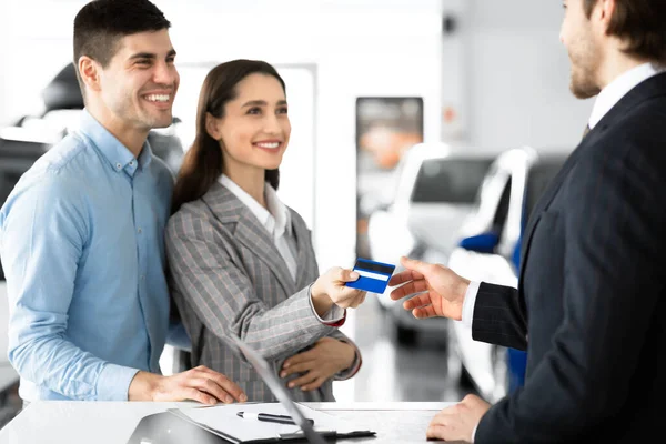 Casal de compra de carro dando cartão de crédito vendedor em Dealership Office — Fotografia de Stock