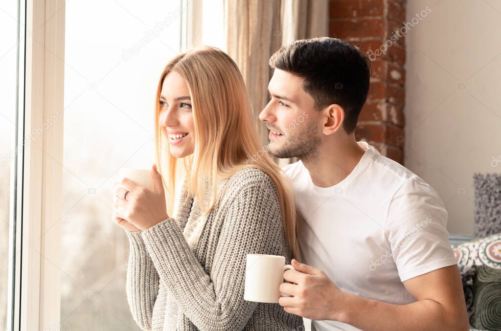 Real love. Smiling man and woman cups of coffee looking out of window in morning