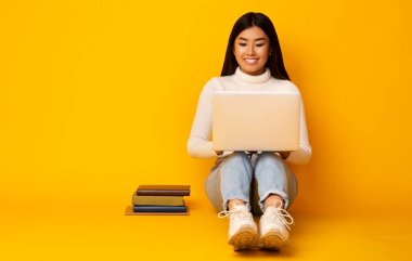 Asian Girl Using Laptop Studying Sitting On Floor In Studio