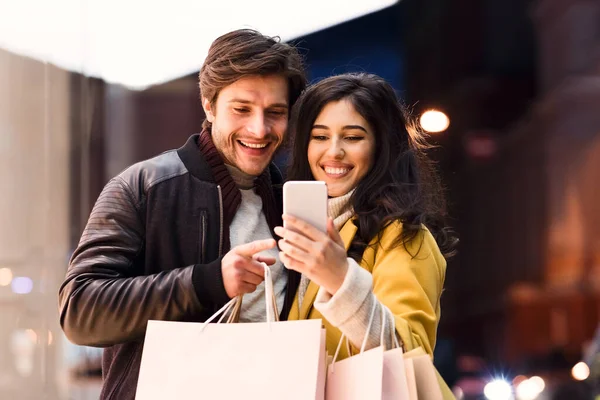 Loving couple using phone after shopping in mall