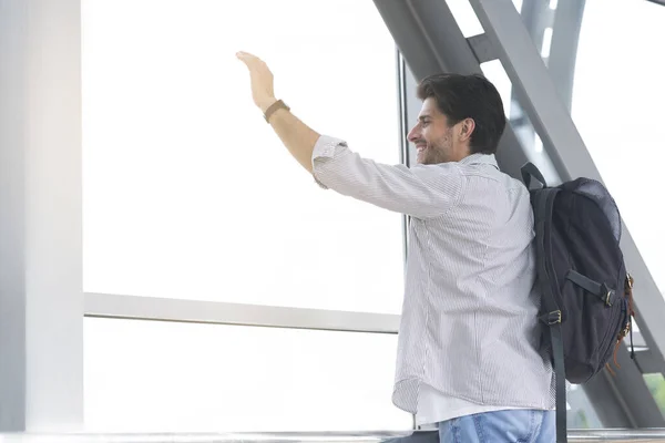 Después de la llegada. Hombre feliz saludando la mano desde la ventana en la terminal del aeropuerto — Foto de Stock