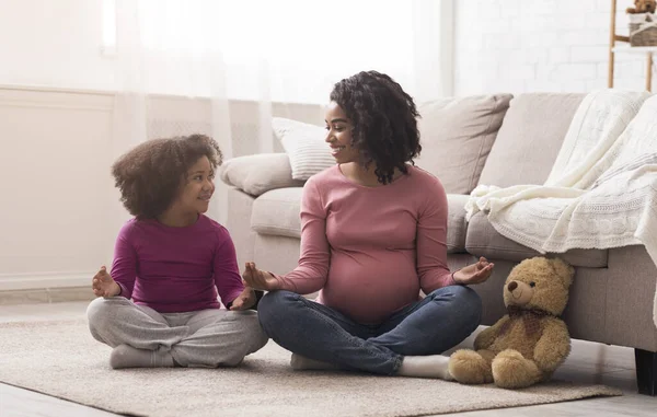 Pregnant black mother and her little daughter practicing youga at home — Stock Fotó
