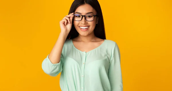 Asiatique fille dans les lunettes de vue posant sourire à la caméra, fond jaune — Photo