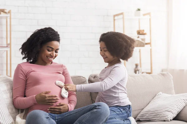 Speels weinig afro meisje zetten baby shoes naar zwanger moeders buik — Stockfoto