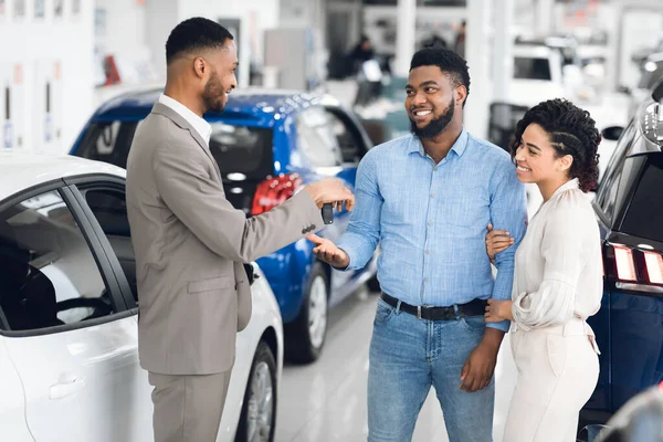 Autohändler übergibt Schlüssel an glückliches Familienpaar im Autohaus — Stockfoto